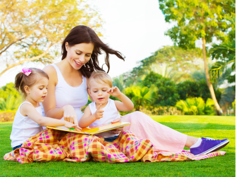芝生の上で絵本を読む女性と子供2人