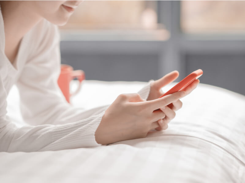 白いベッドの上でスマートフォンを操作する女性