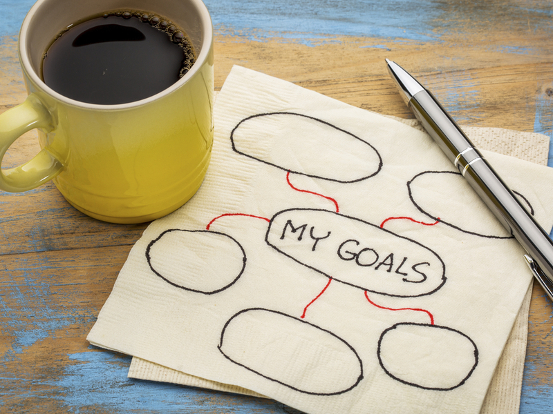 「MY GOALS」と書かれたナプキンとコーヒーが入った黄色のマグカップ