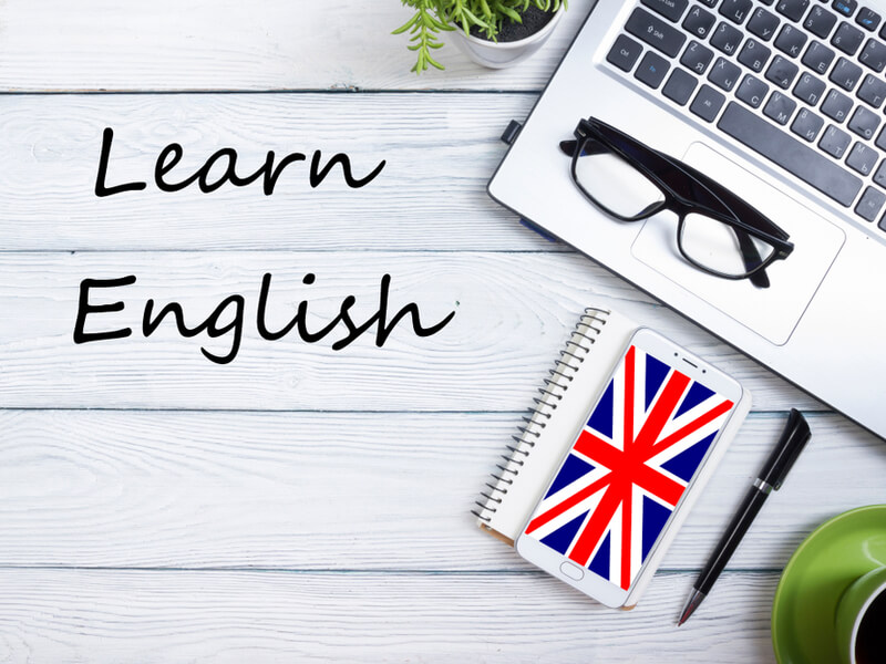 「Learn English」と書かれた木目のテーブルとパソコン、メガネ、ノート