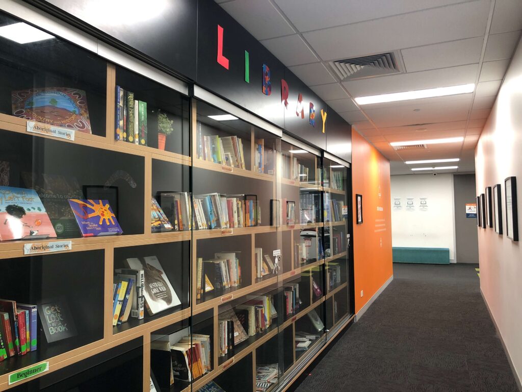 ILSC Sydneyのキャンパス内にある図書スペースと廊下の様子（本棚と明るいオレンジ壁が特徴）
