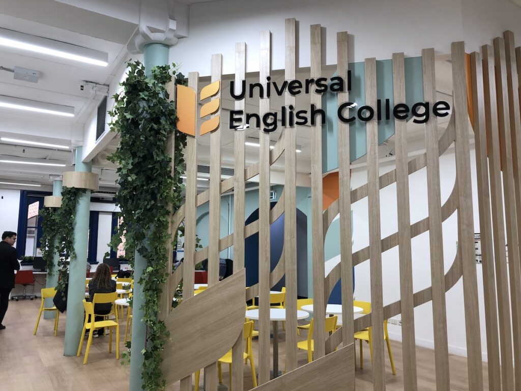 Universal English Collegeシドニー校の校内ラウンジの様子。木目のパーティションと観葉植物が配置された明るい空間で、黄色の椅子が並ぶ開放的な雰囲気が伝わる。