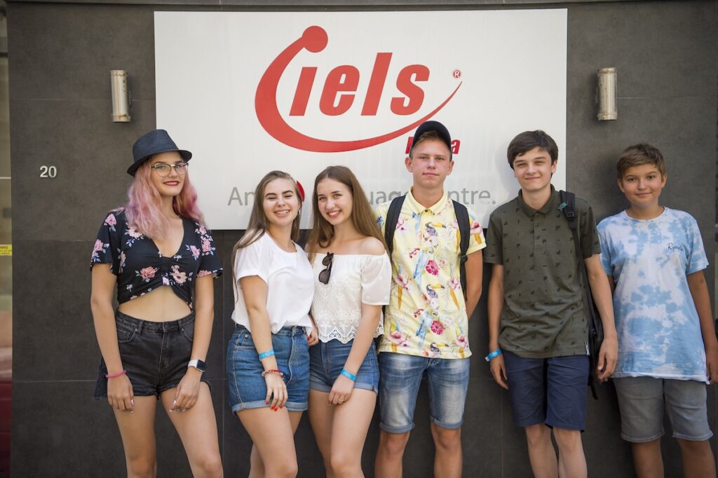 IELSのYoung Learner Program参加者が、学校のロゴ前で集合写真を撮影している様子