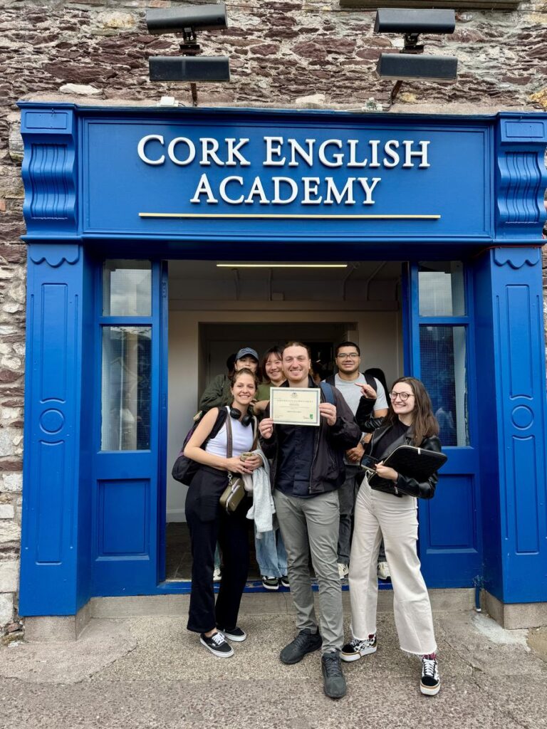 Cork English Academyの正面入口（ブルーの看板）で修了証を持つ学生たち